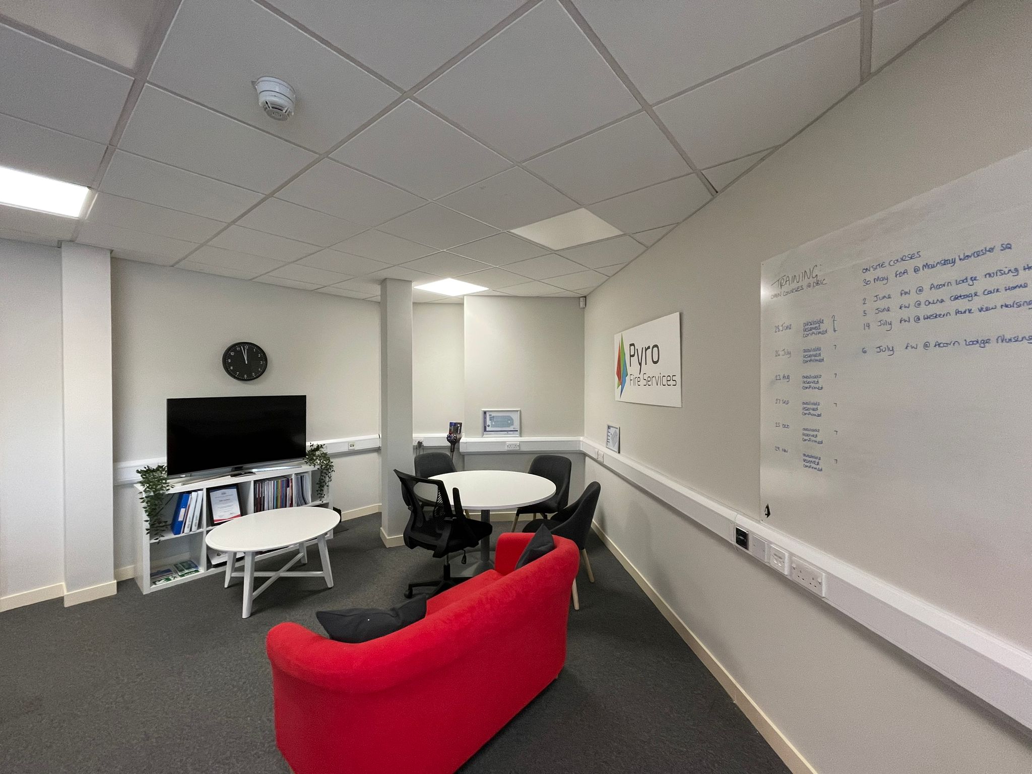 The Pyro Fire office before the redesign: a breakout area with a red sofa, a round meeting table and a whiteboard on a bare wall