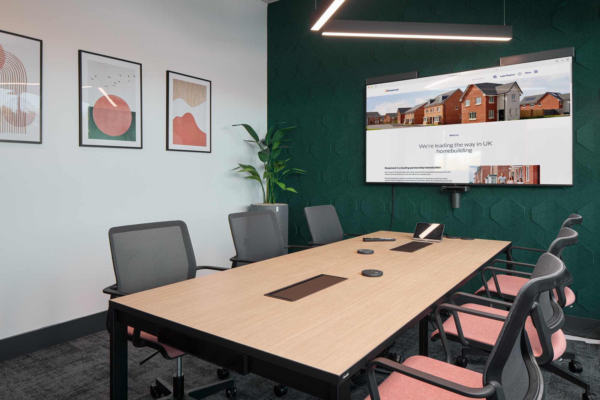 A meeting room with a dark green acoustic panelled wall, a timber table and a wall-mounted screen