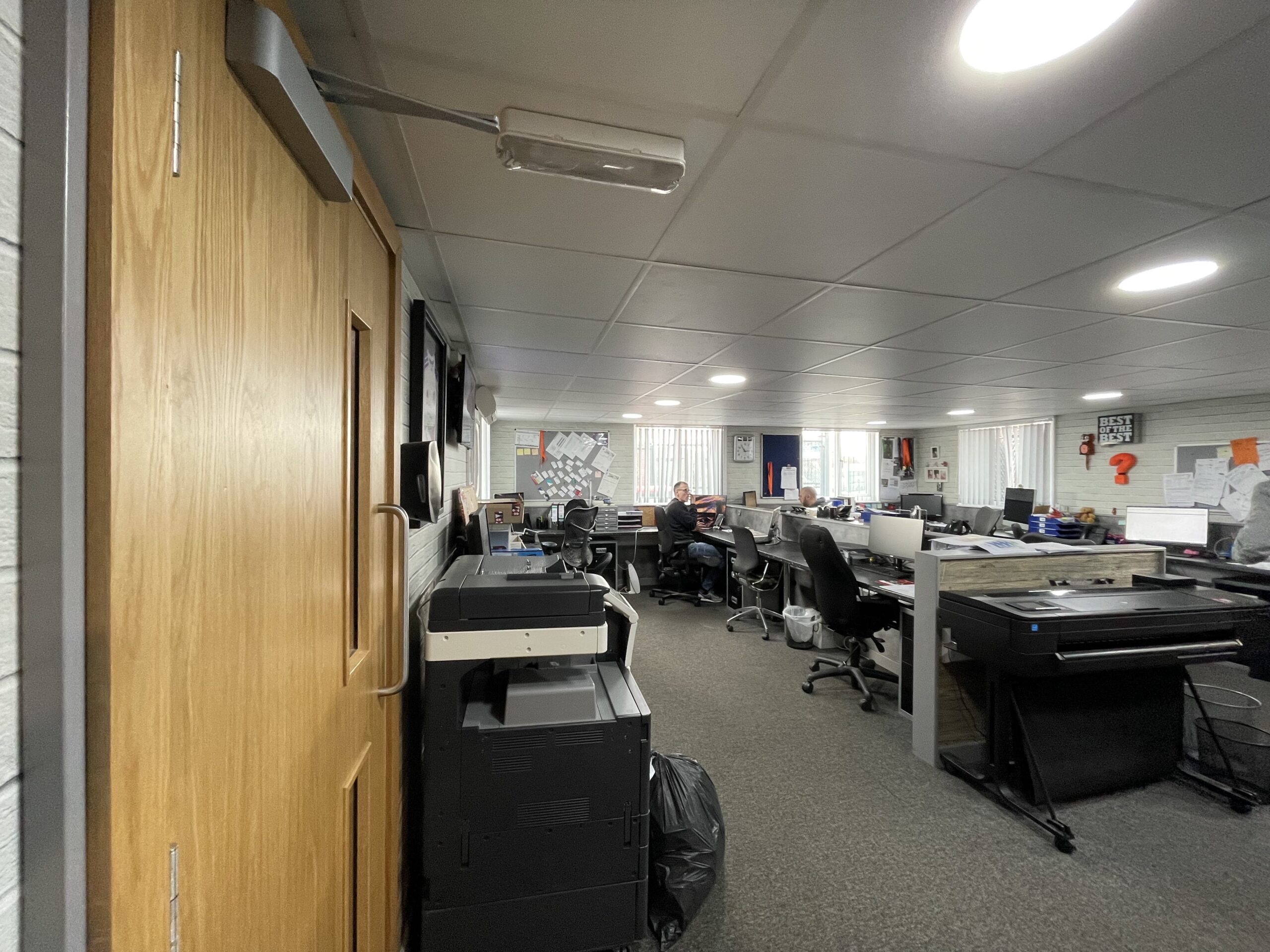 The Gray and Sons office before the redesign, seen through a doorway, with printers and rows of desks