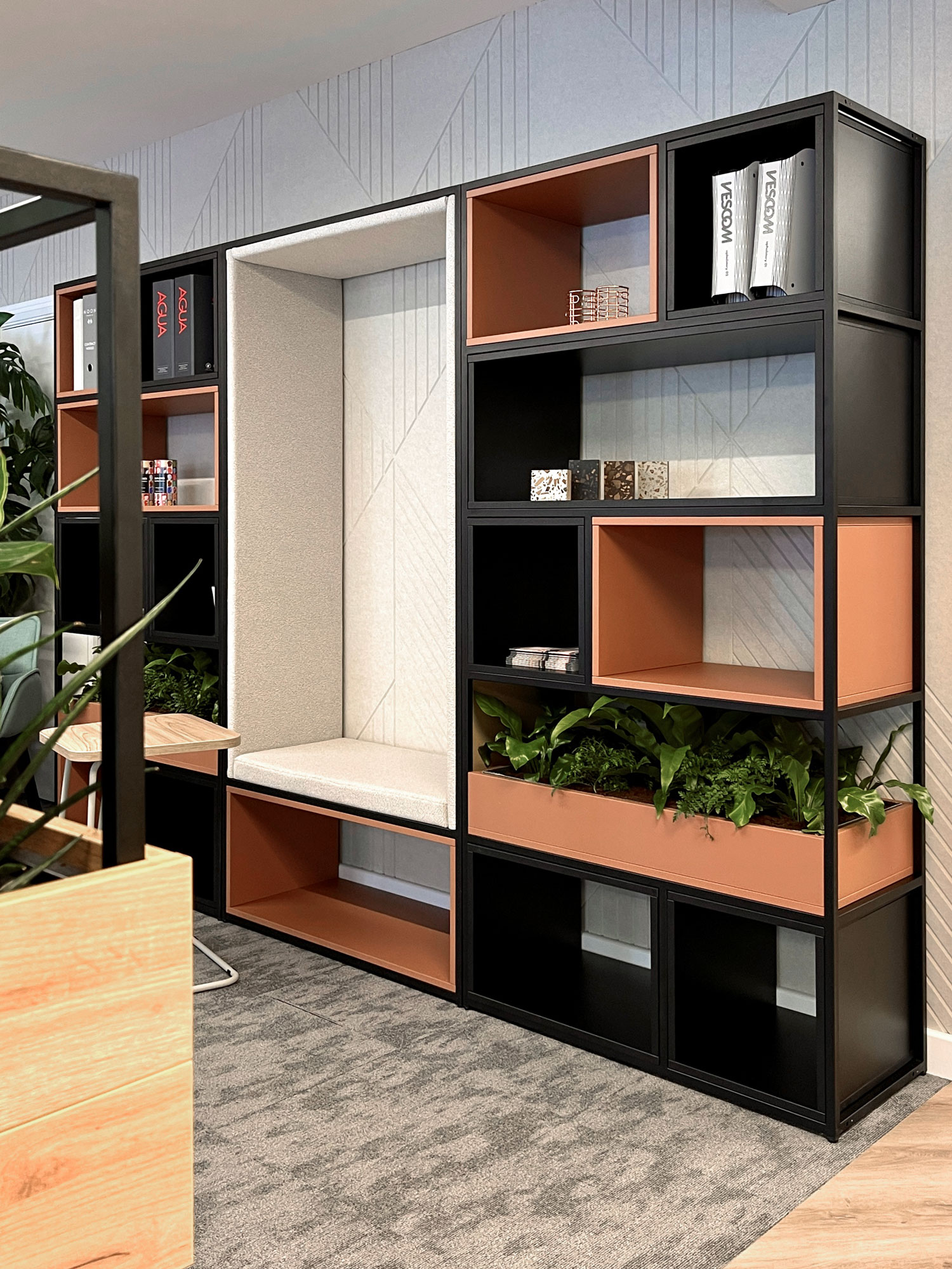 A black and orange storage unit with open shelving and planting, used to divide an office
