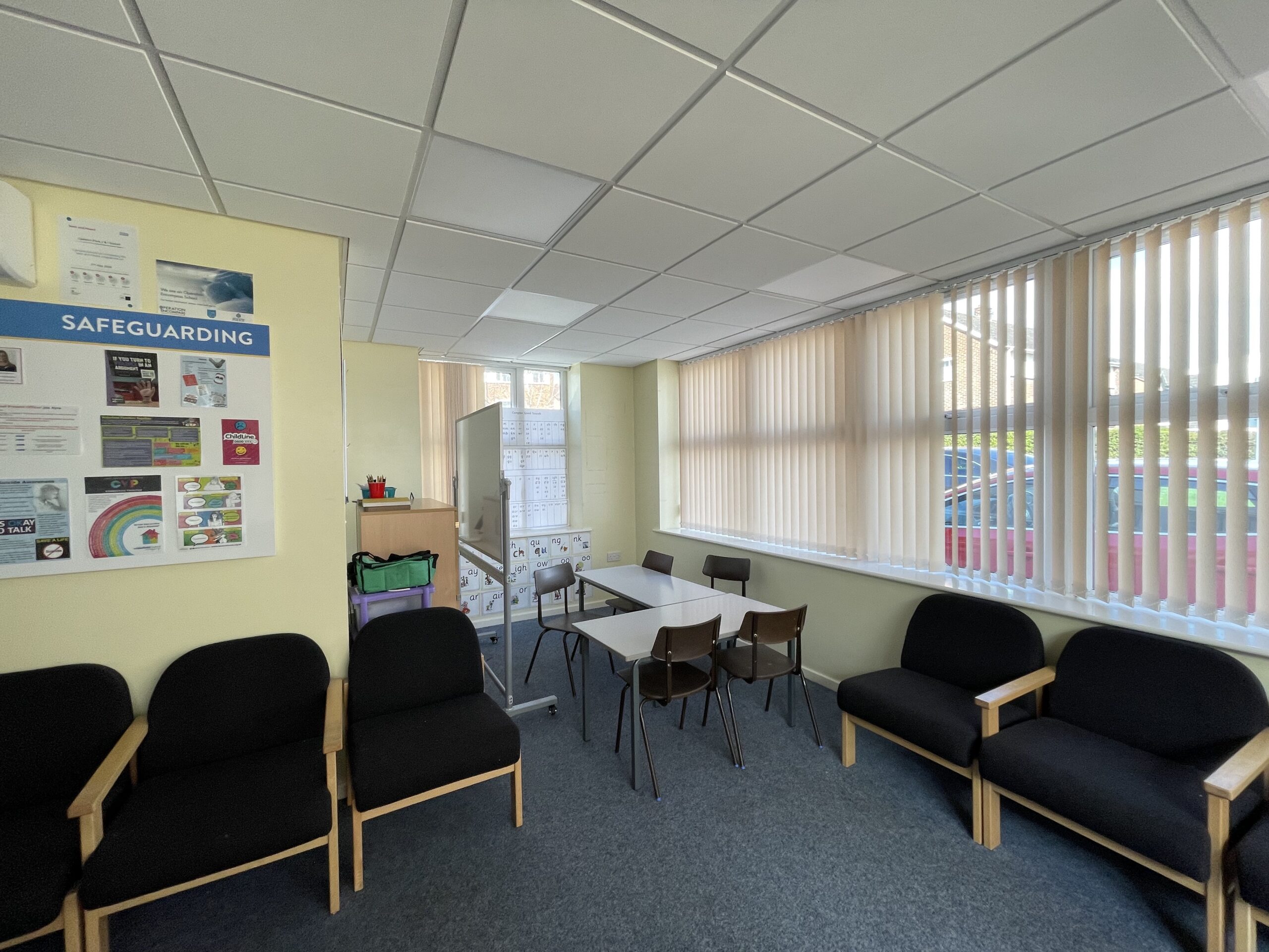 A meeting room at the school before the refresh, with black framed chairs and a safeguarding noticeboard