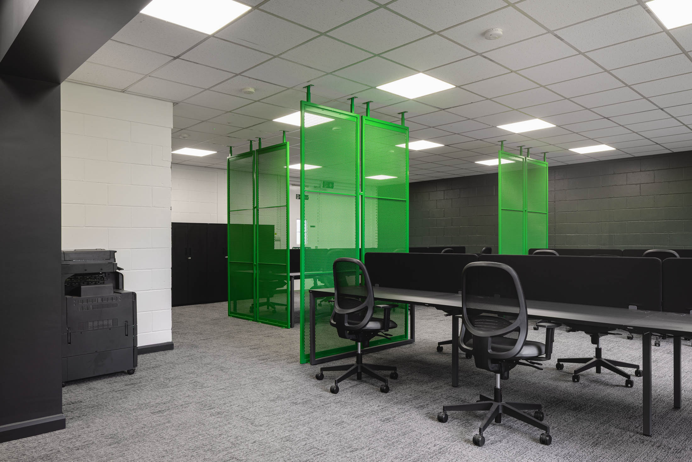 A London office with green framed glazed pods enclosing meeting space beside open plan desks