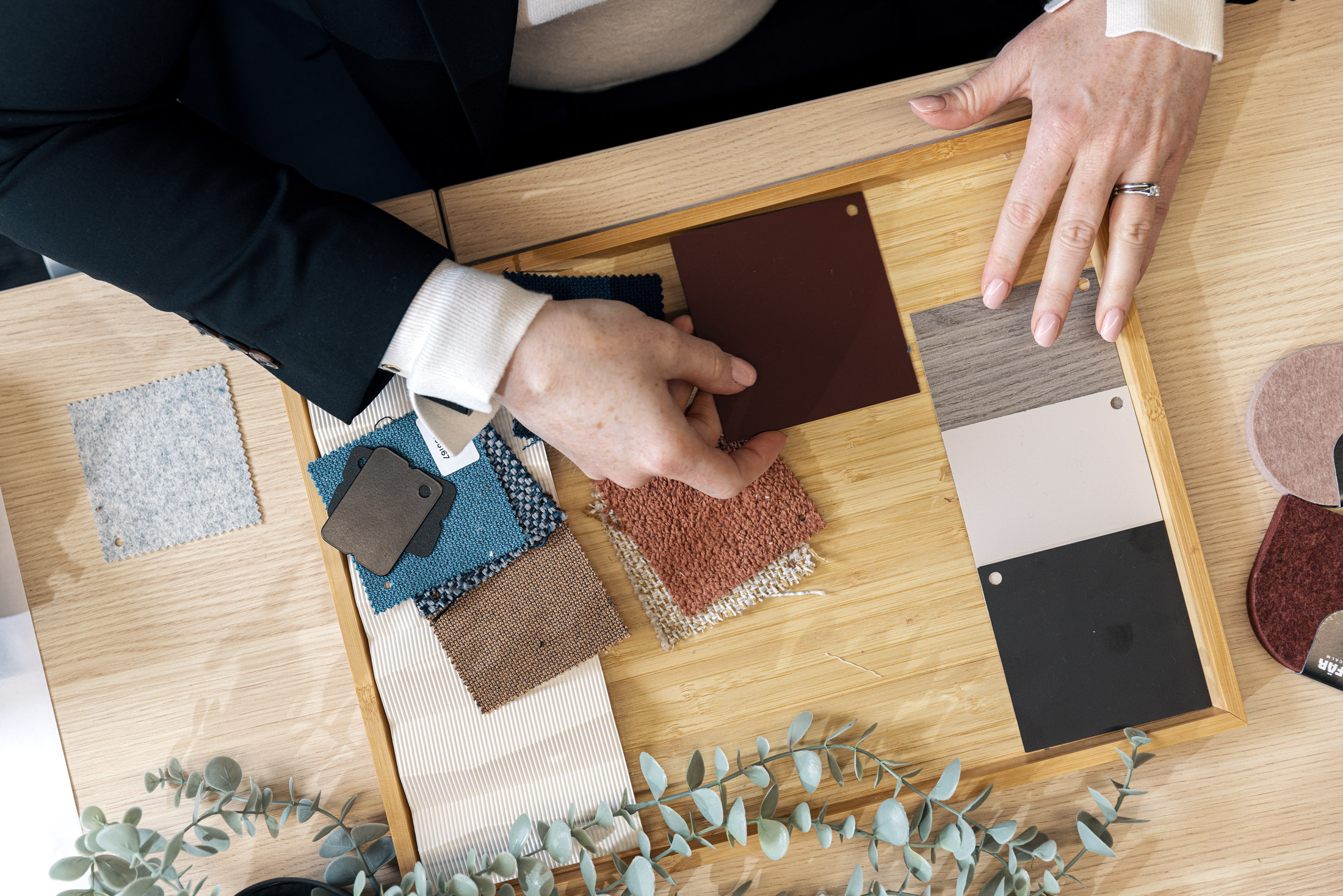 Hands arranging fabric, timber and carpet samples on a tray as a material palette