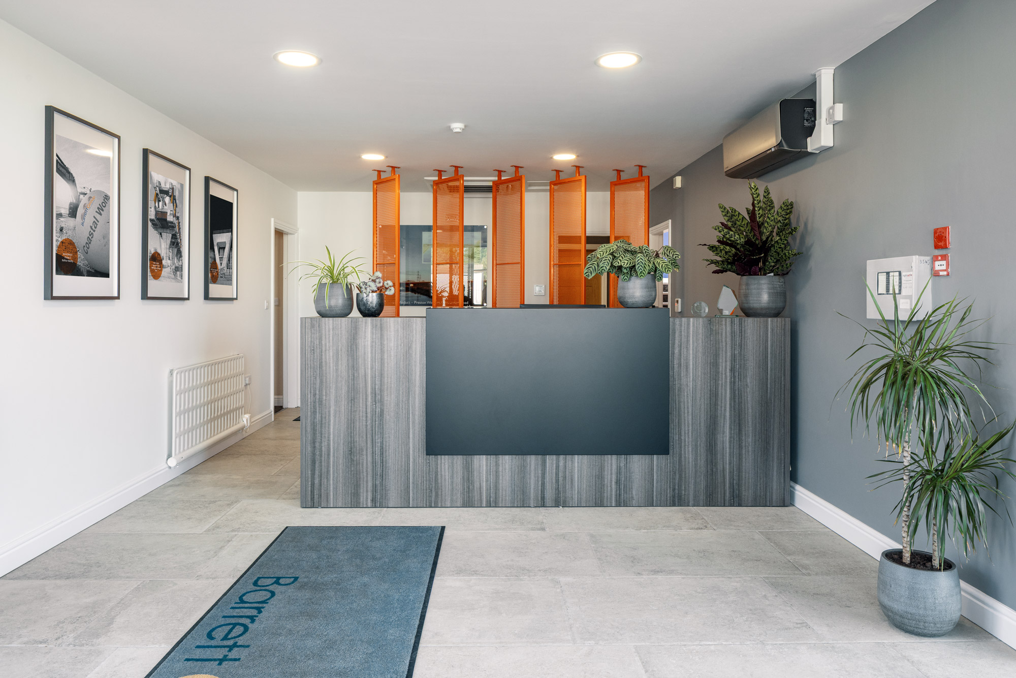The new reception at Barrett Group, with orange mesh screens behind the desk and a branded entrance mat