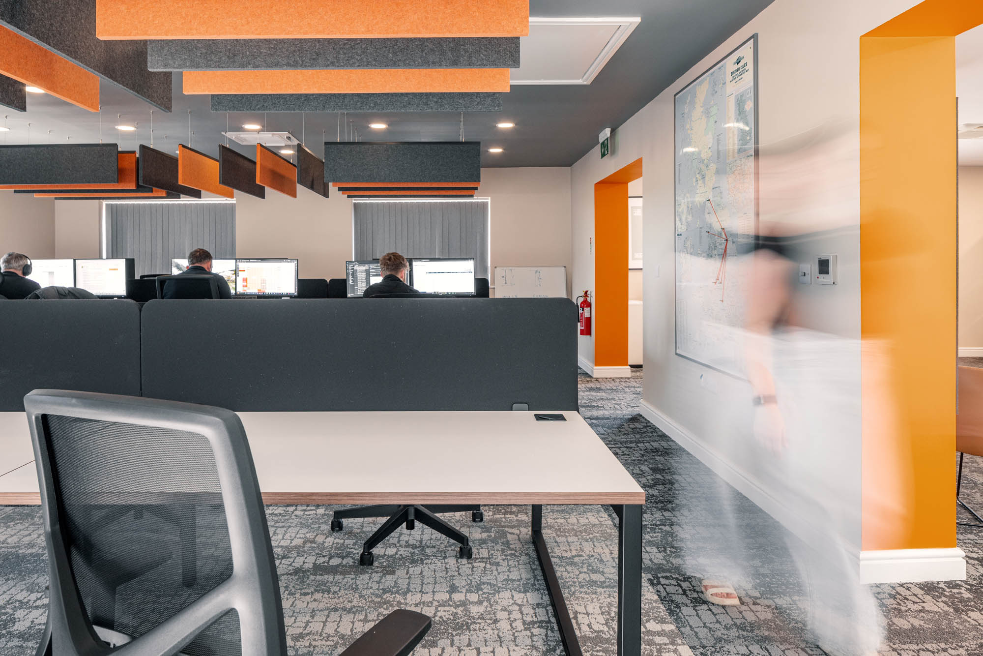 Open plan office with orange and grey acoustic baffles above the desks