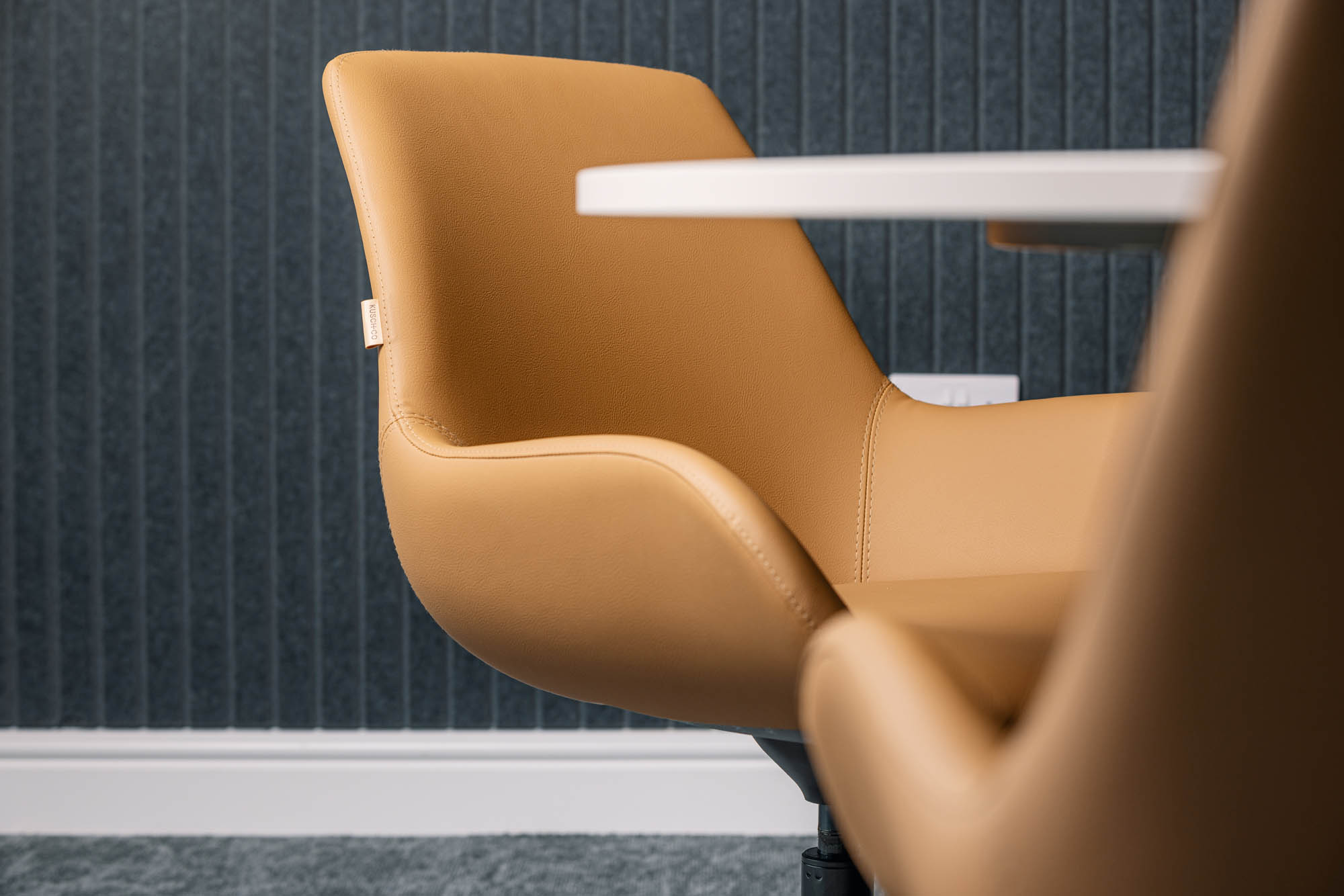 A tan leather boardroom chair against a ribbed wall panel