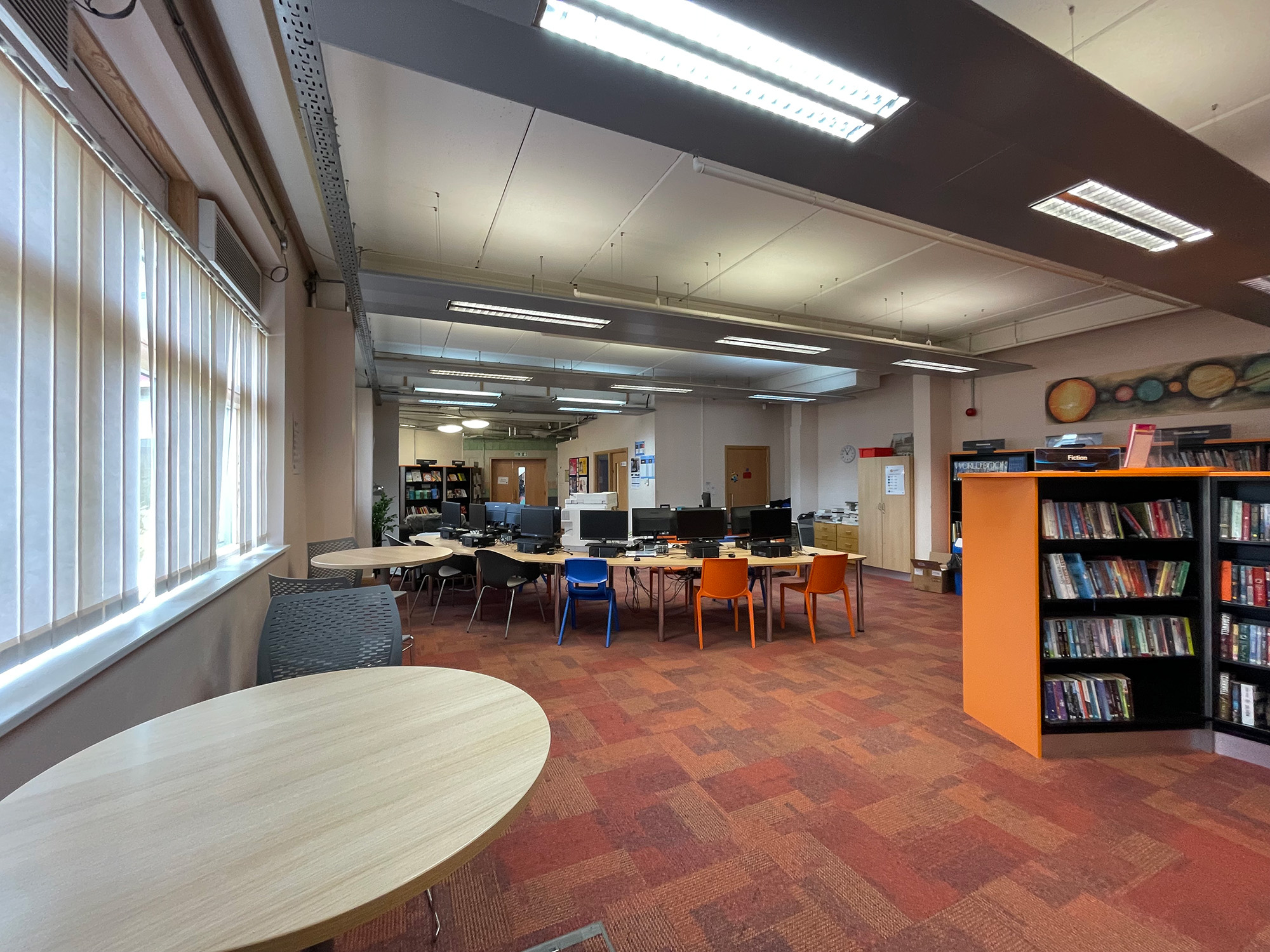 The original library before the redesign, with red carpet tiles, strip lights, an oval table and a row of computers