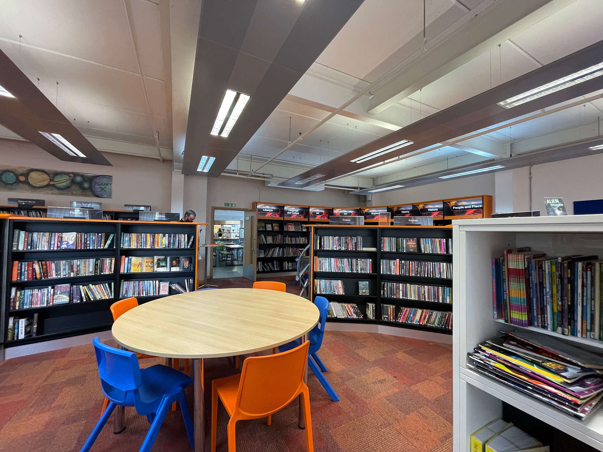The original library before the redesign, with a round table, blue and orange chairs and black bookshelves